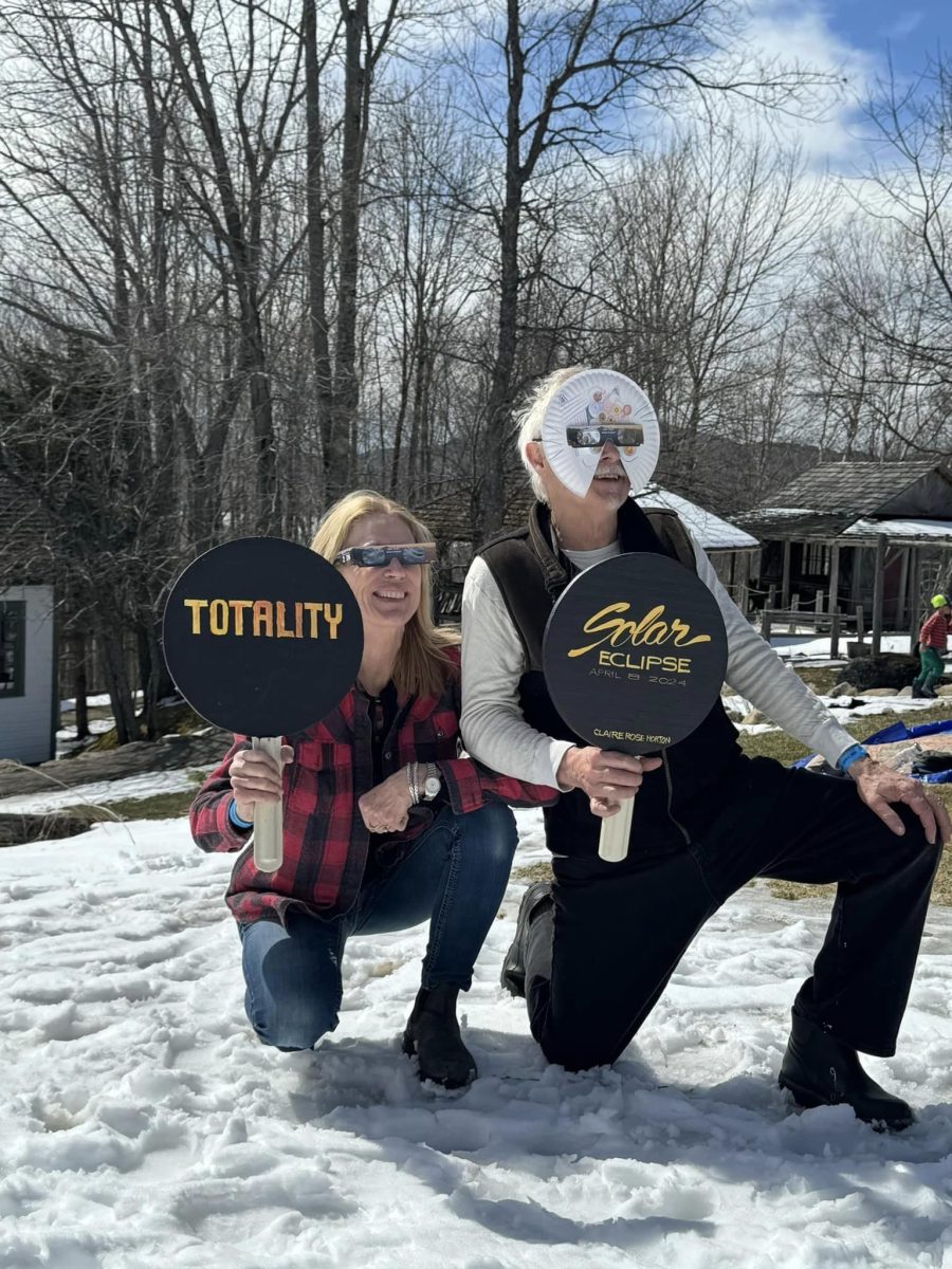 Two people wear eclipse glasses and hold up signs